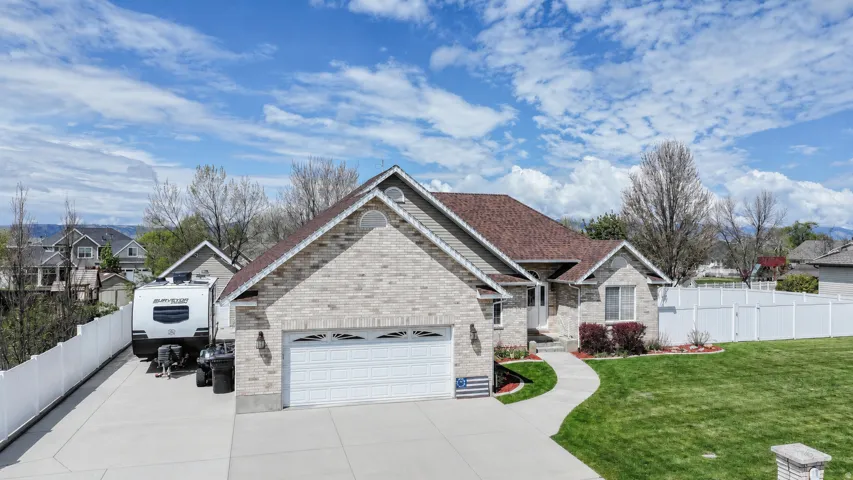 Traditional-style residence featuring a brick and siding exterior, an attached garage, a long concrete driveway, and a white privacy fence encompassing the property