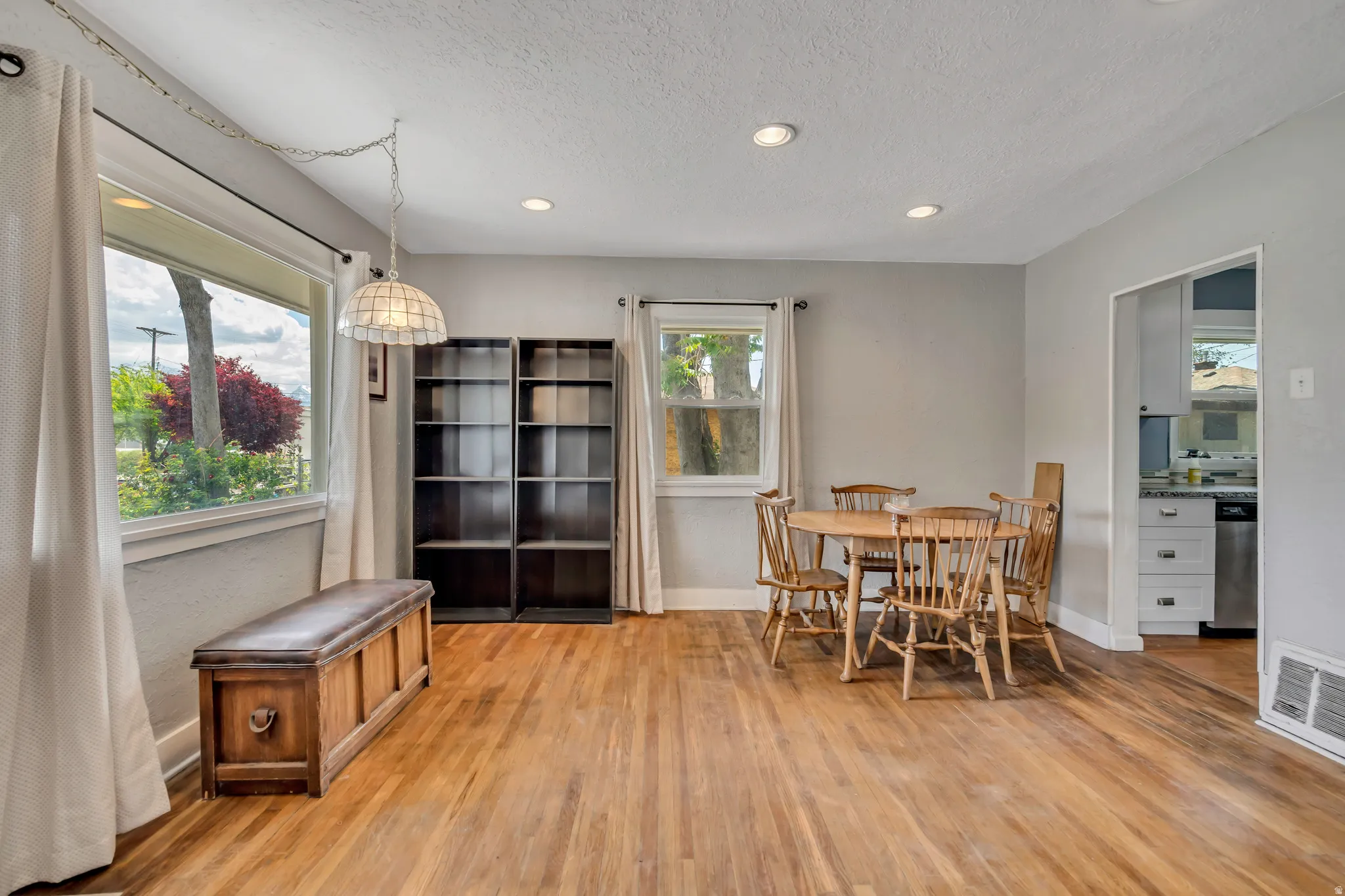 Light-filled living space featuring wood-finish flooring, recessed lighting, and a kitchen entry