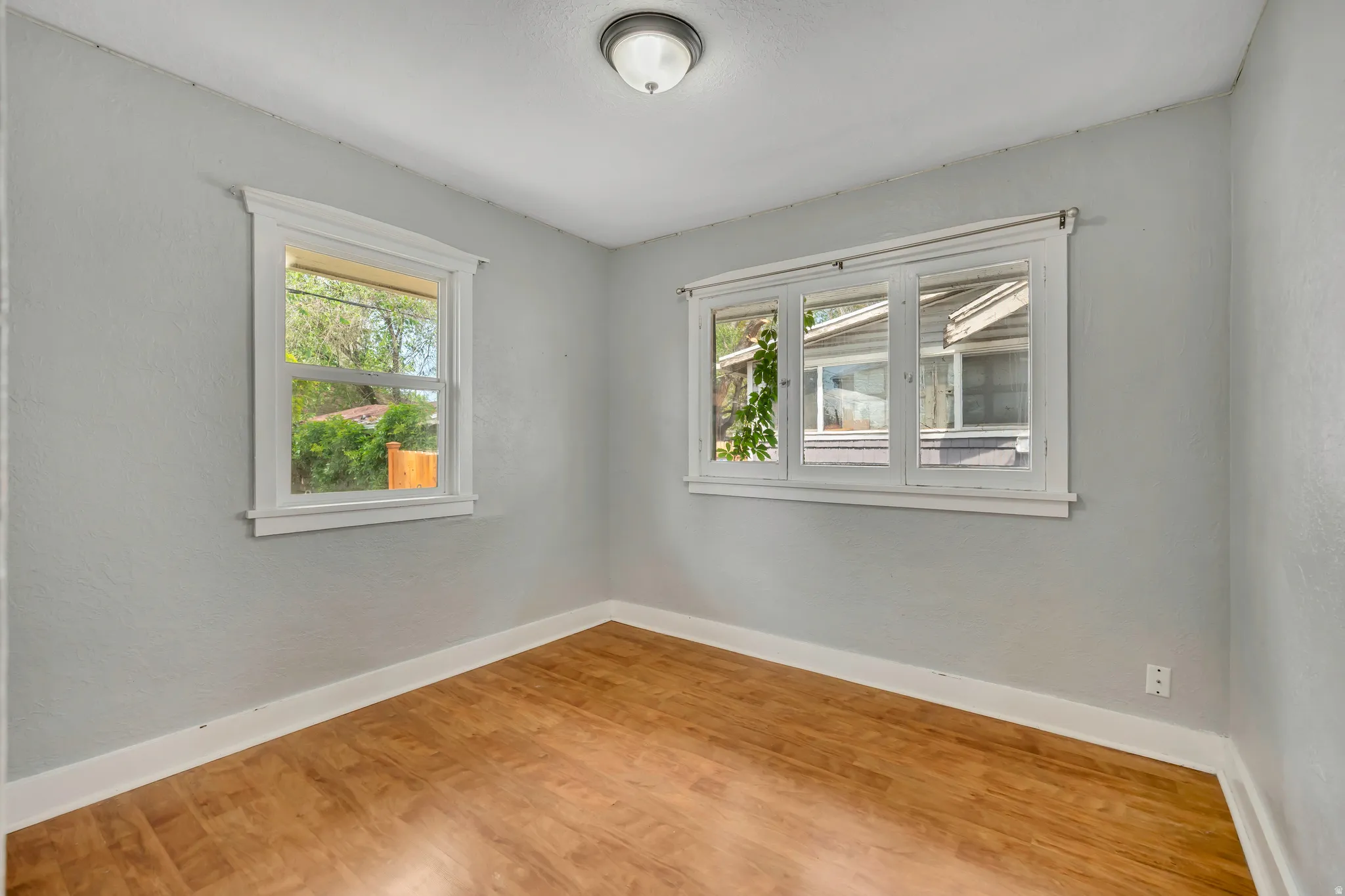 Light-filled room featuring wood-finish flooring, white baseboards, and two windows with white trim