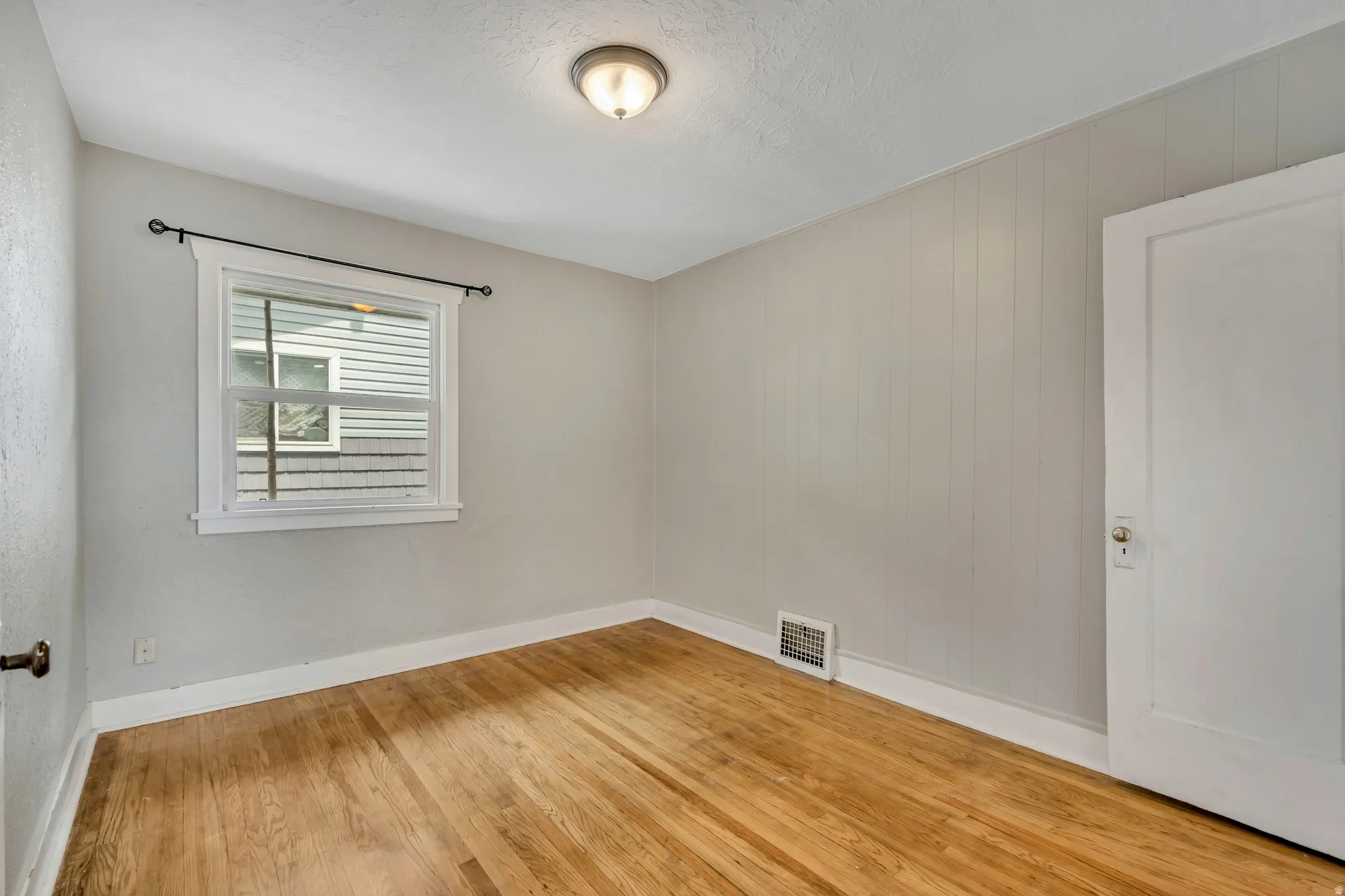 Bedroom featuring wood-finish flooring, white trim, a double-hung window, wall paneling, and a flush-mount ceiling light