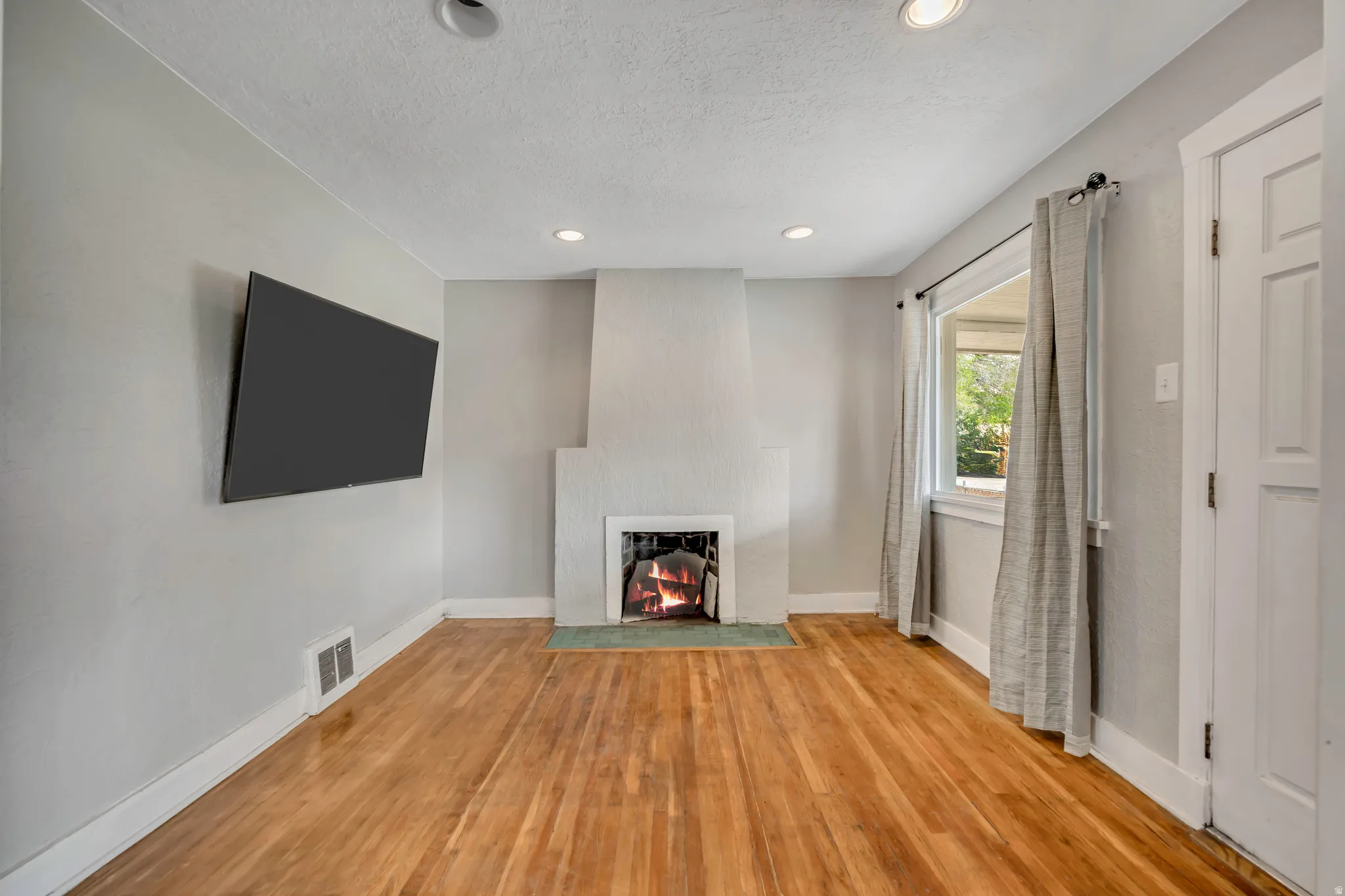 Living area featuring wood-finish flooring, a fireplace with a light-colored surround, recessed lighting, and a wall-mounted television