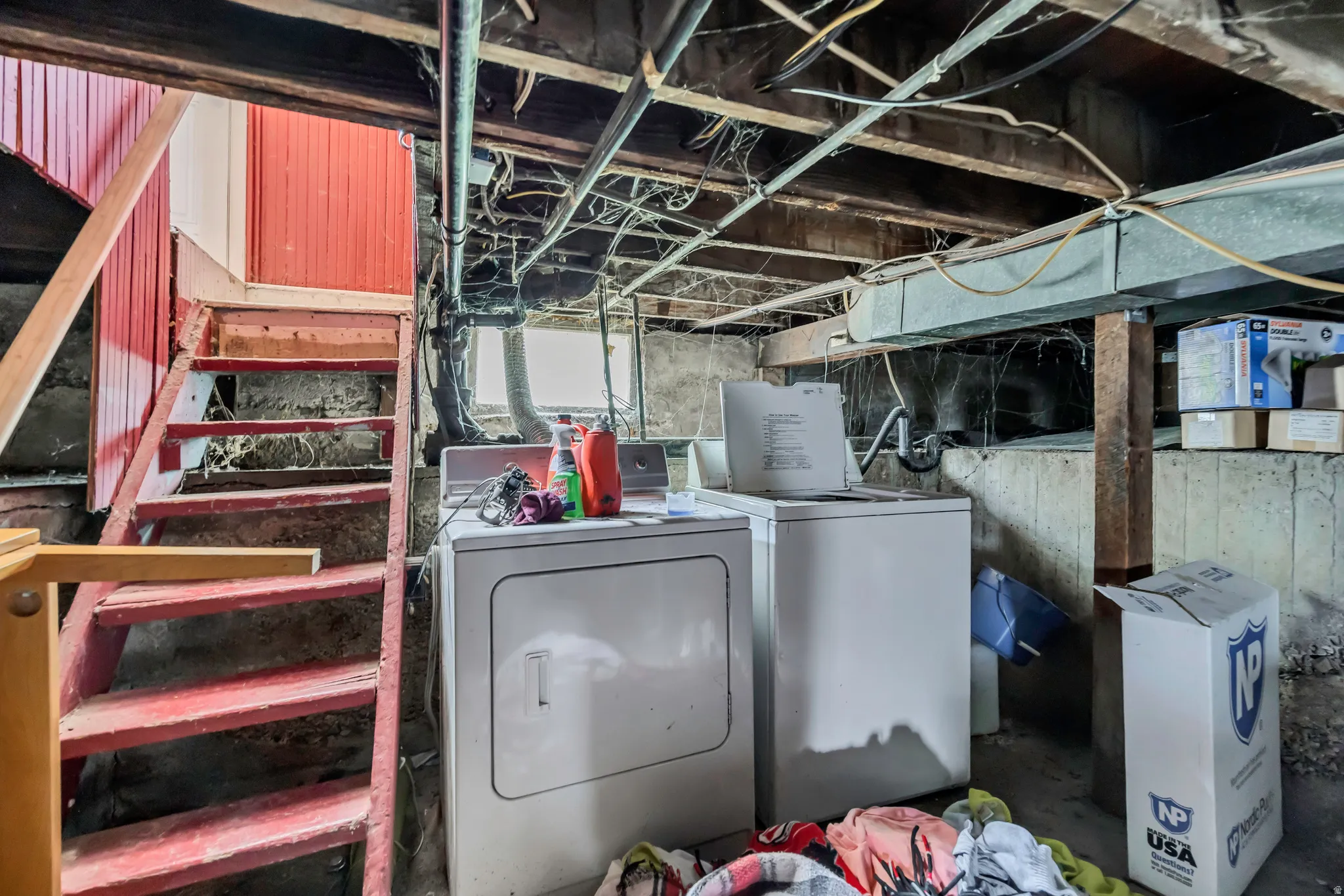 Basement utility area featuring exposed joists, concrete walls, a wooden staircase with red painted risers, and an installed washer and dryer unit