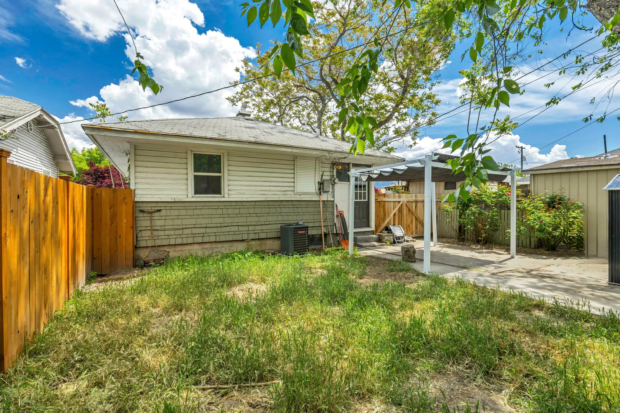 Backyard featuring a covered patio structure, partial wood fencing, and a concrete driveway