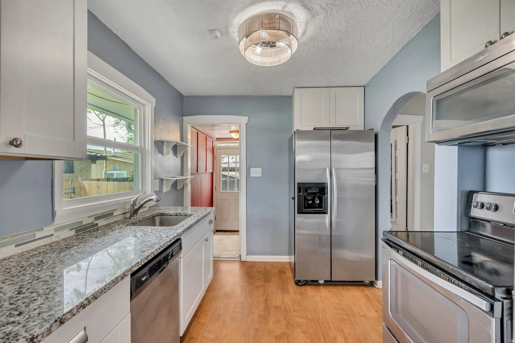 Kitchen featuring light wood-finish flooring, white cabinetry, speckled countertops, a double basin sink with a gooseneck faucet, and stainless steel appliances including a refrigerator, dishwasher, and stove