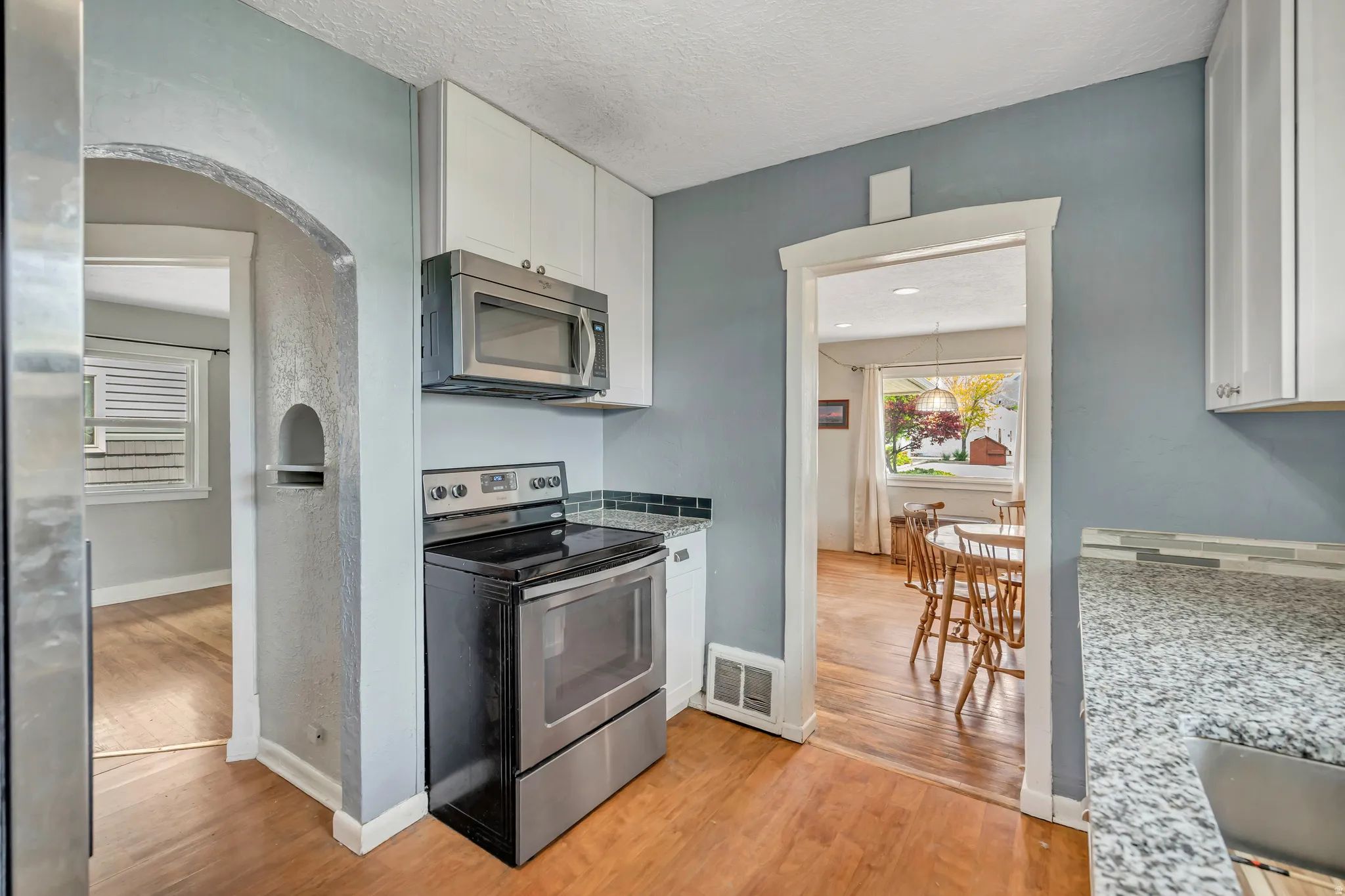 Kitchen featuring a stainless steel range, built-in microwave, white cabinetry, and granite-finish countertops
