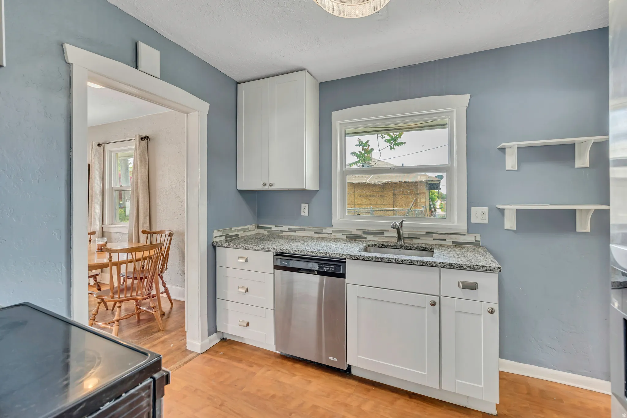 Kitchen featuring white cabinetry, a stainless steel dishwasher, a countertop with an integrated sink, a tile backsplash, and wood-finish flooring