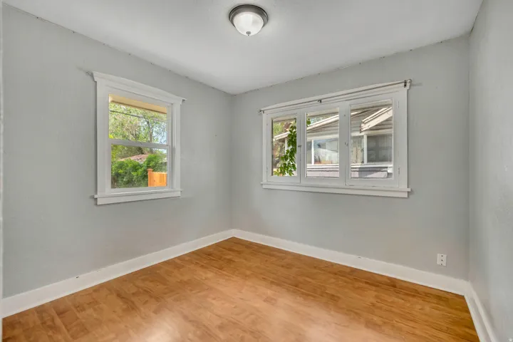 Light-filled room featuring wood-finish flooring, white baseboards, and two windows with white trim