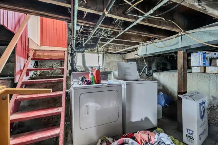 Basement utility area featuring exposed joists, concrete walls, a wooden staircase with red painted risers, and an installed washer and dryer unit