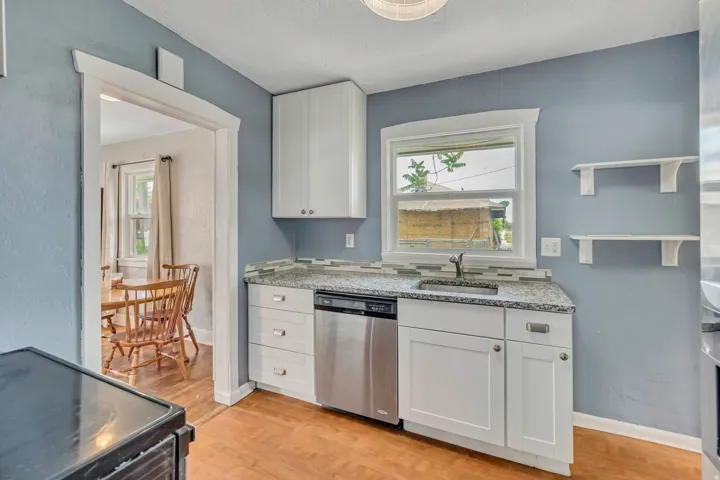 Kitchen featuring white cabinetry, a stainless steel dishwasher, a countertop with an integrated sink, a tile backsplash, and wood-finish flooring