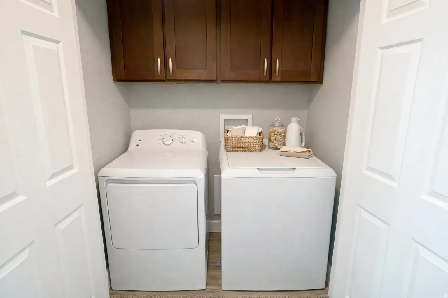 Dedicated laundry area featuring wood-finish flooring and upper cabinetry with silver hardware