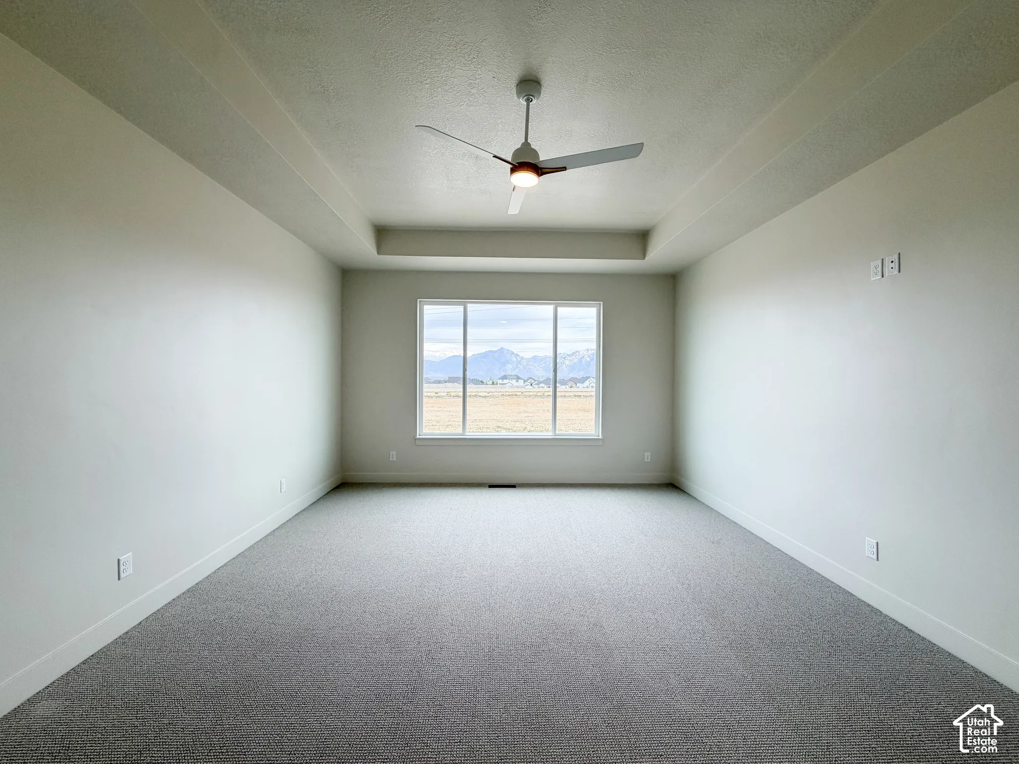 Spacious primary  bedroom featuring a tray ceiling, ceiling fan, large window, and light gray carpeting