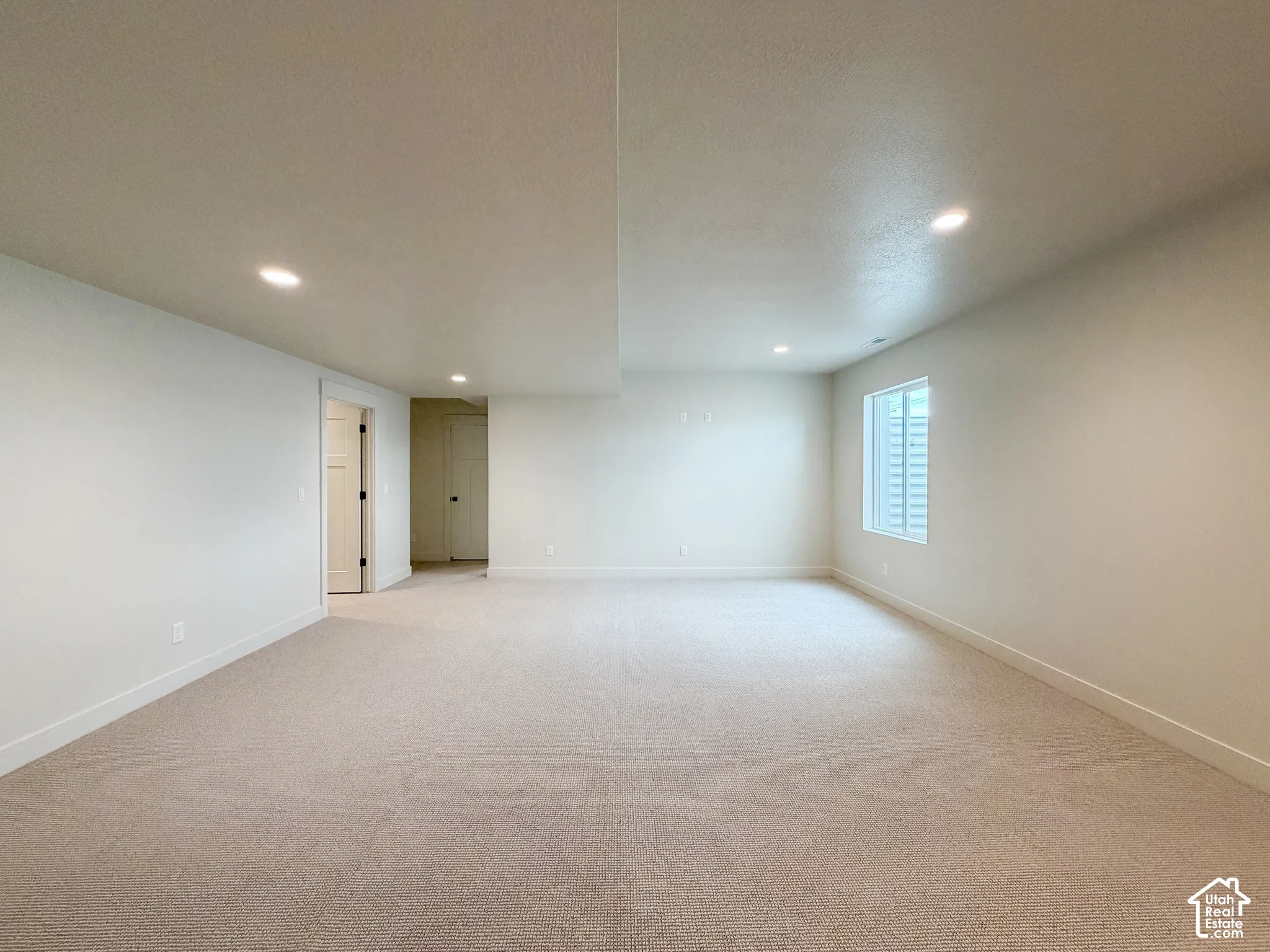 Expansive carpeted room with neutral wall tones, recessed lighting, and a window with a light well