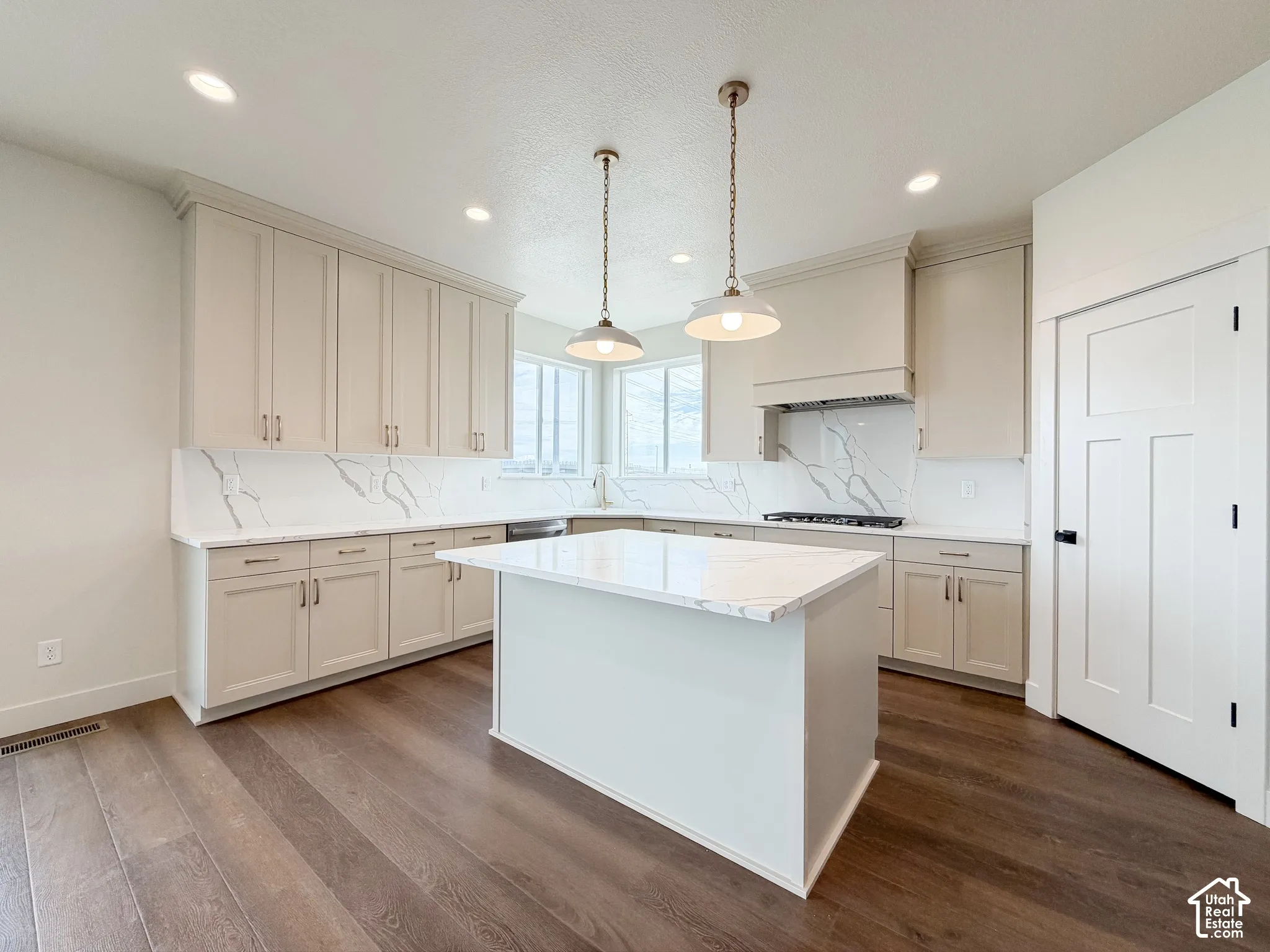Kitchen featuring wood-finish flooring, an island with a white countertop, light-toned cabinetry, and a white backsplash with gray veining