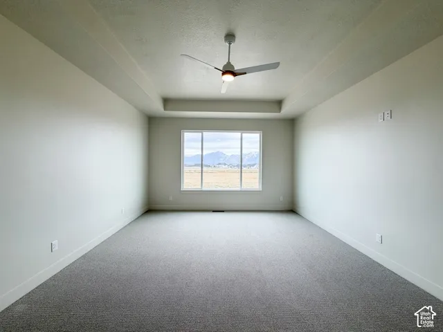 Spacious primary  bedroom featuring a tray ceiling, ceiling fan, large window, and light gray carpeting