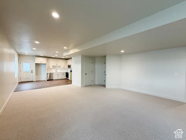 Open-concept living area with plush carpeting, recessed lighting, and a modern kitchen featuring white cabinetry, stainless steel appliances, and wood-finish flooring