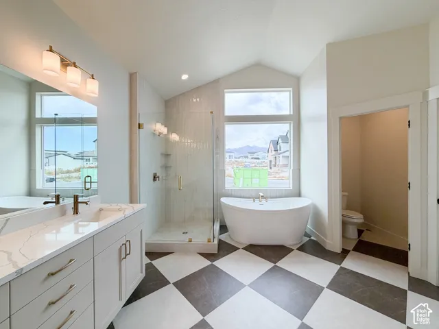 Vaulted ceiling bathroom featuring a freestanding tub, glass-enclosed shower with tile surround, dual vanity with quartz countertop, and checkerboard floor tiling