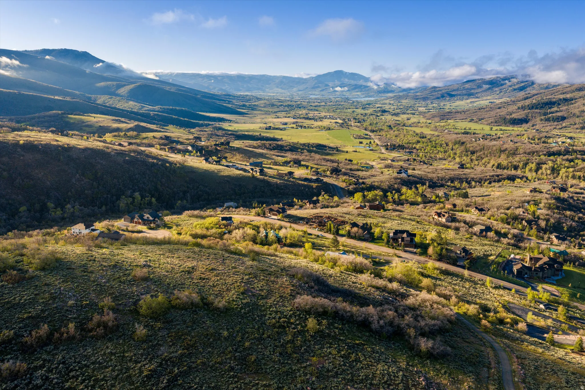 Expansive valley landscape featuring rolling hills, distant mountains, and scattered residential properties