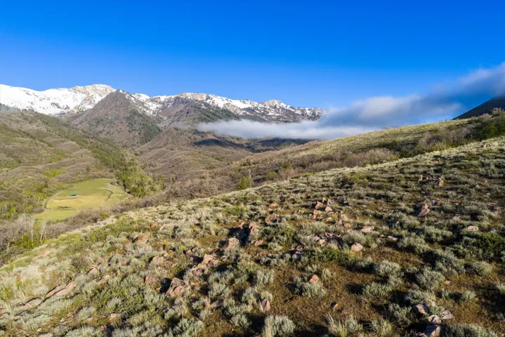 Expansive mountain landscape featuring varied terrain, a clear blue sky, and distant snow-capped peaks