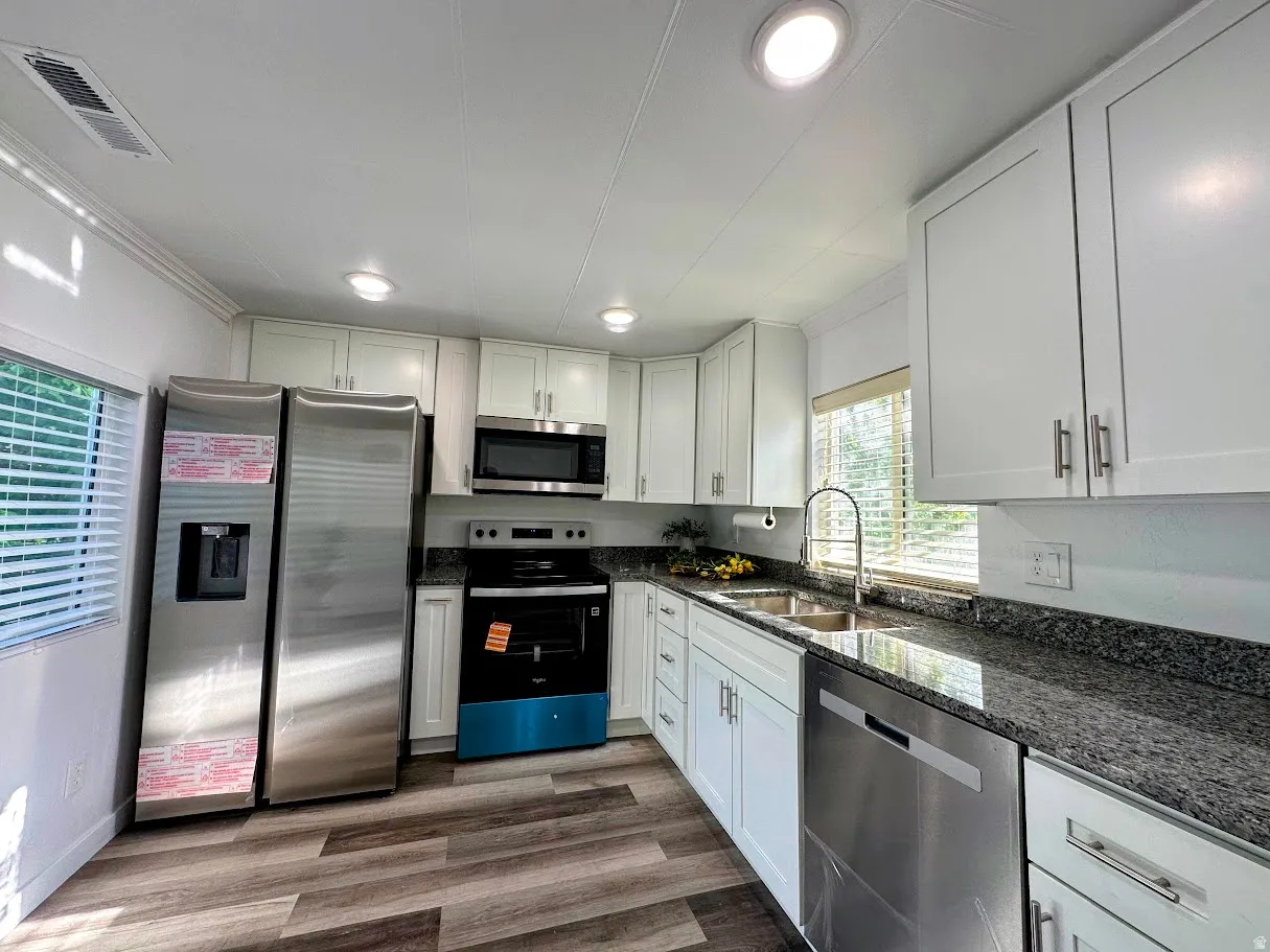 Modern kitchen featuring white cabinetry, dark granite countertops, and stainless steel appliances including a refrigerator, microwave, range, and dishwasher