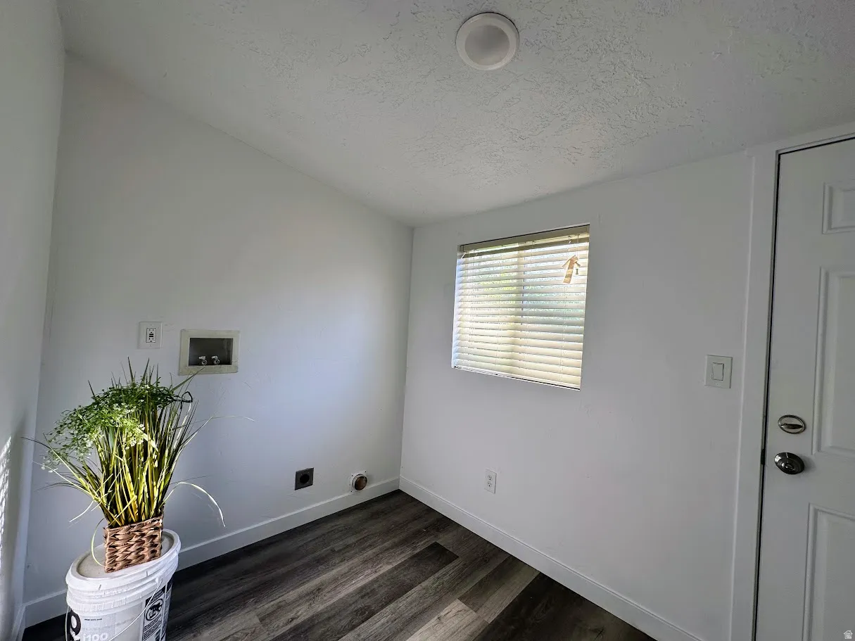 Laundry area featuring wood-finish flooring, white walls, and a window with blinds