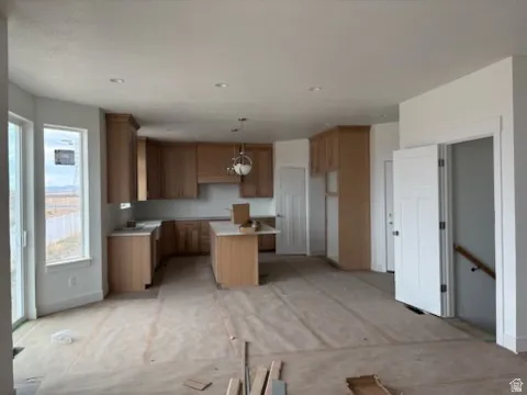 Open-concept kitchen featuring light wood cabinetry, a central island, recessed lighting, and a pendant light fixture