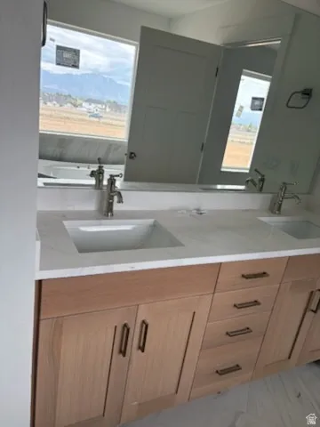 Double vanity featuring light wood-finish cabinetry with matte black hardware, integrated rectangular sinks, and a light-toned countertop