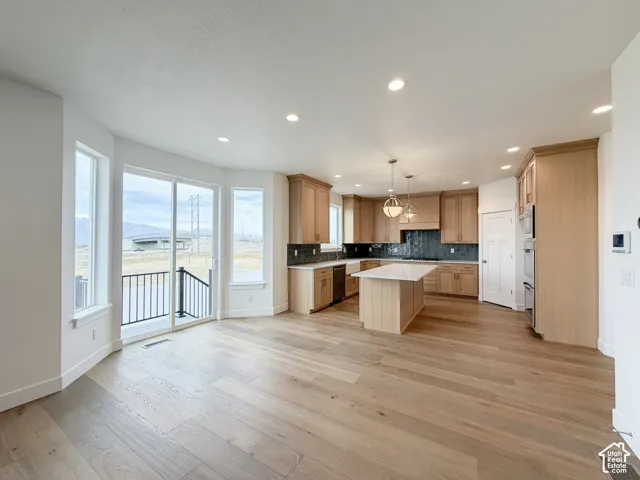Spacious kitchen featuring light wood-finish cabinetry, a large center island with a white countertop, and integrated stainless steel appliances
