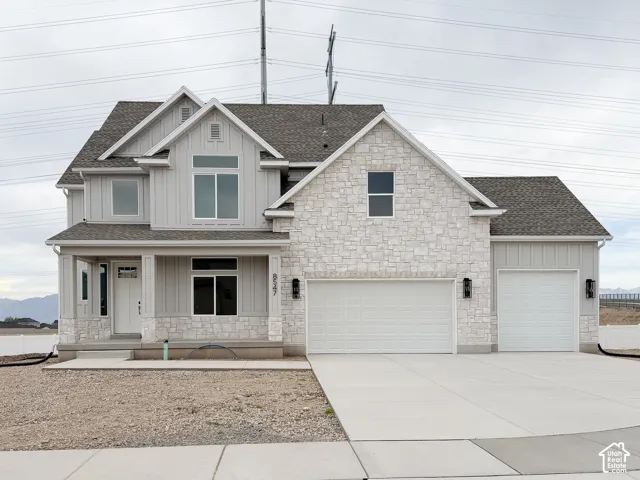 Contemporary exterior featuring a stone and board-and-batten facade, covered entry, and attached multi-car garage with two separate doors
