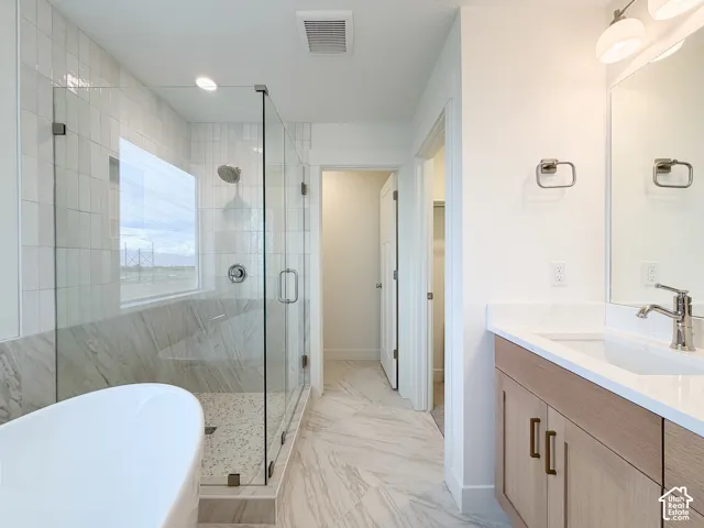 Freestanding tub, glass-enclosed shower with tiled walls, dual-sink vanity with light wood-finish cabinetry, and large format tile flooring