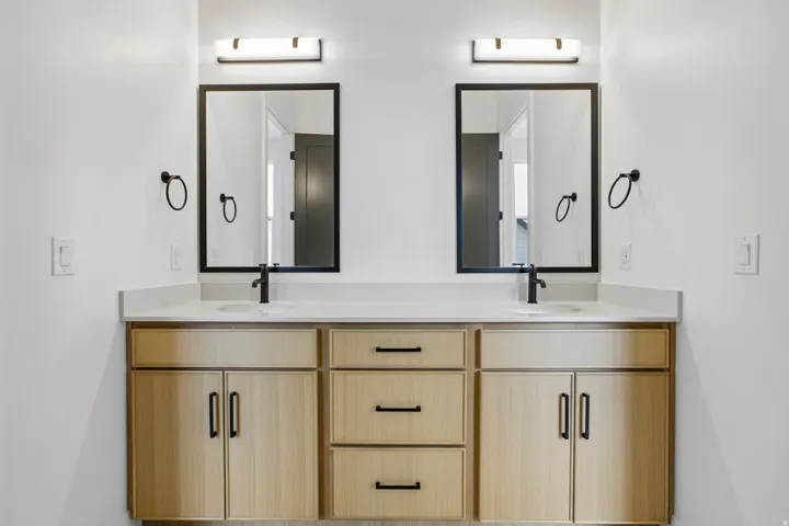 Dual vanity with light wood-finish cabinetry, white countertop, individual rectangular mirrors, and matte black hardware