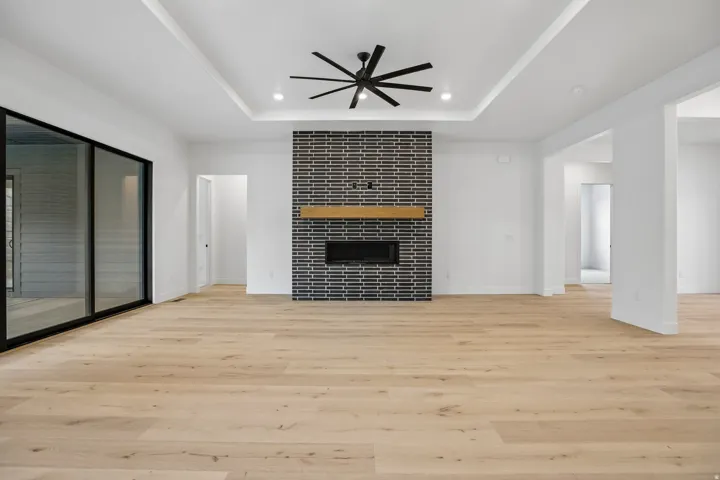 Tray ceiling with recessed lighting and a ceiling fan, black brick fireplace surround with a wood-finish mantel, wide-plank wood-finish flooring, and large sliding glass doors