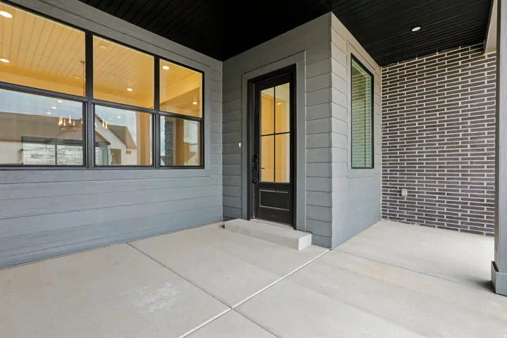 Concrete patio with dark horizontal siding, dark brick accent wall, and a dark entry door with glass panels