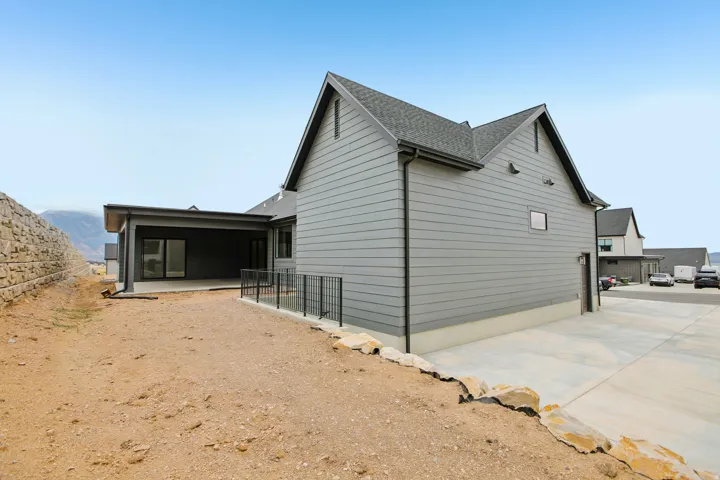 Covered patio with concrete flooring, dark gray siding, black metal railing, and a retaining wall