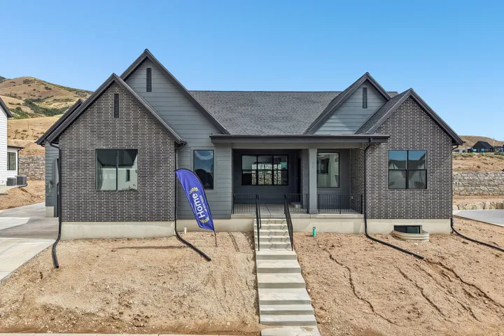 Modern exterior featuring dark gray siding, brick accents, a covered entry porch with black railings, a dark shingle roof, and a concrete pathway leading to the entrance