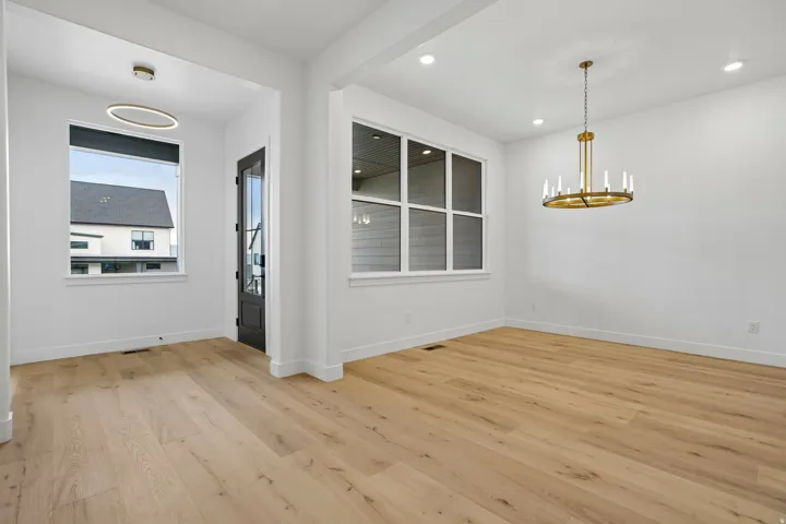 Open-concept space featuring light wood-finish flooring, white walls, large windows, and a modern brass chandelier