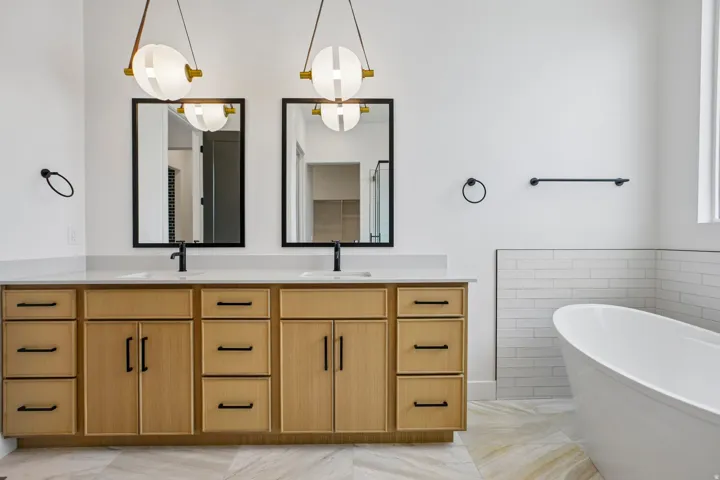 Double vanity with light wood-finish cabinetry, dual undermount sinks, and matte black fixtures