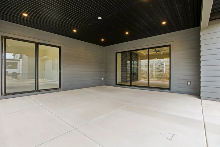 Covered patio featuring a slatted ceiling with recessed lighting, two sets of sliding glass doors, and gray horizontal siding