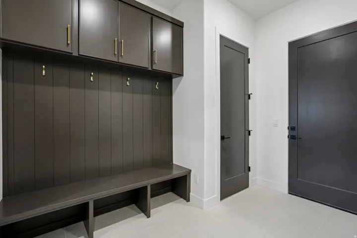 Built-in bench seating with integrated storage, overhead cabinetry featuring brass hardware, plank wall paneling with brass hooks, and two dark panel doors