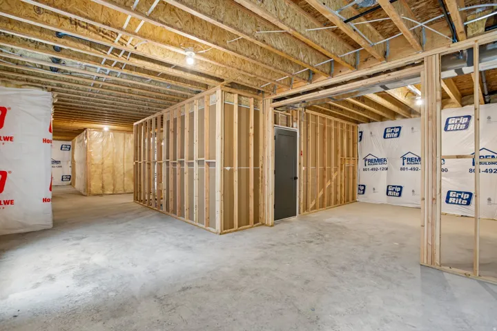 Unfinished basement with concrete flooring, exposed wood framing, and overhead lighting