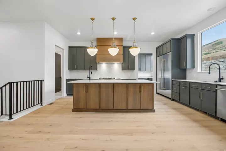 Modern kitchen featuring wood-finish flooring, a central island with integrated storage, dark cabinetry, and stainless steel appliances