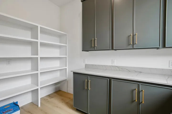 Built-in open shelving, extensive cabinetry with gold-tone hardware, polished countertop, and wood-finish flooring