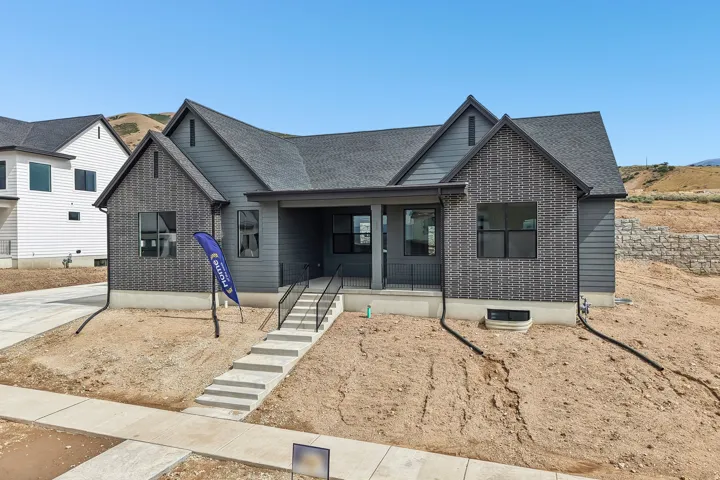 Modern craftsman exterior featuring gray siding, dark gray brick accents, black-framed windows, and a covered porch with black railings
