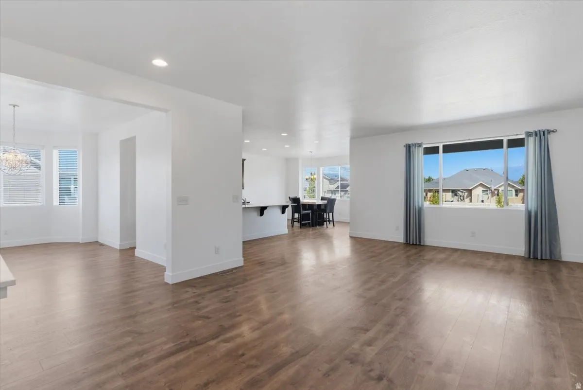 Spacious living area featuring wood-finish flooring, recessed lighting, and a large window with blue drapes