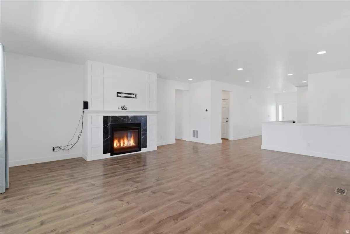 Spacious interior featuring wood-finish flooring, recessed lighting, and a contemporary fireplace with a white mantel and dark stone surround