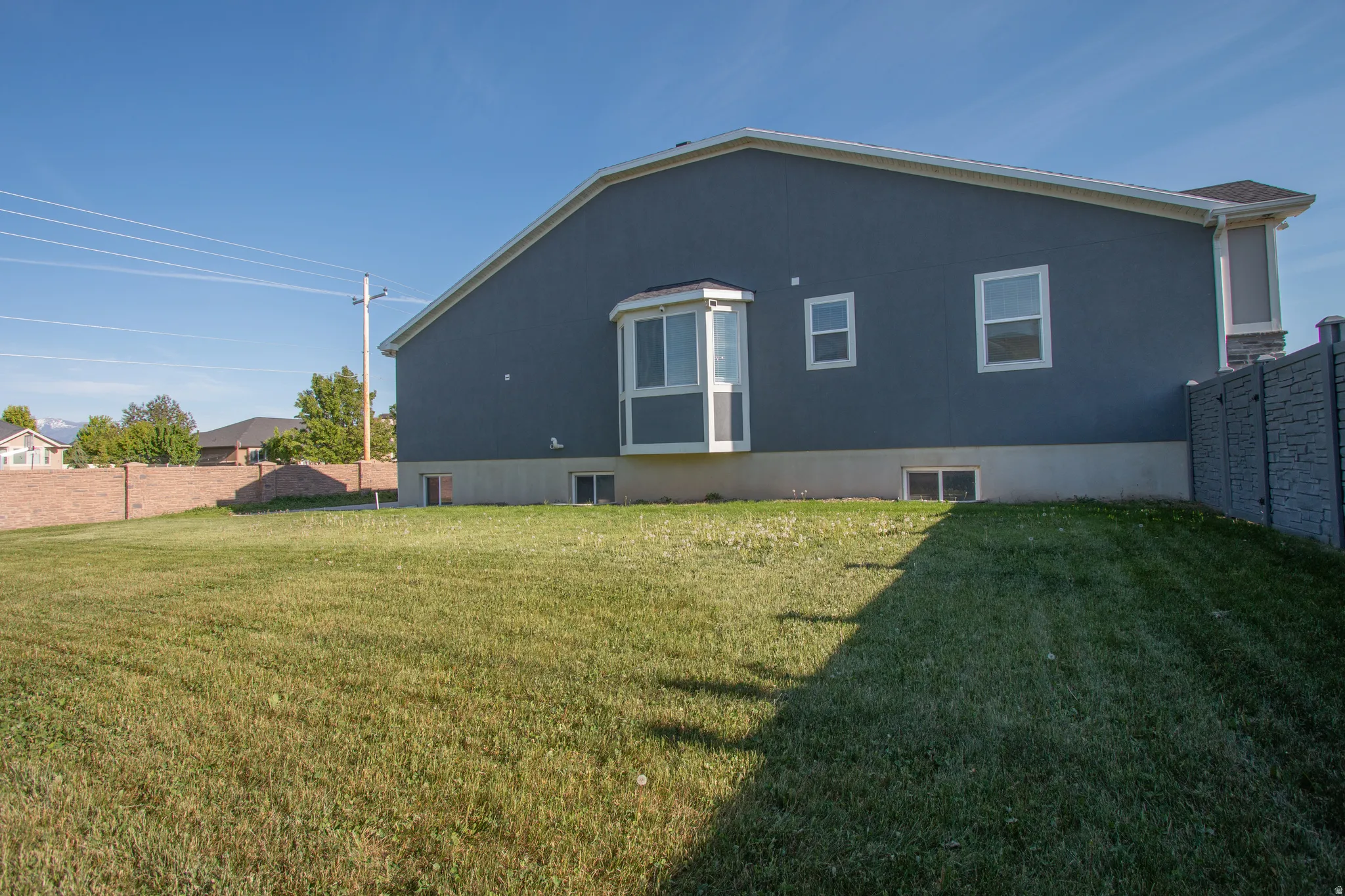 Expansive green lawn bordering the property, featuring a stucco exterior with a bay window and multiple white-framed windows