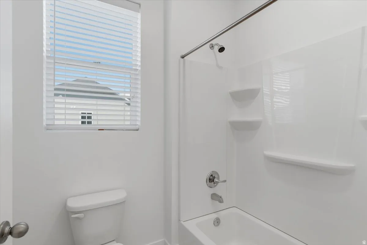 White bathroom featuring a shower-tub combination, chrome fixtures, and a window with horizontal blinds