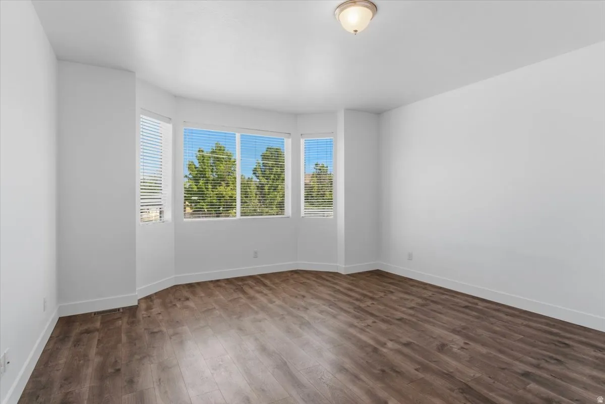 Bright room featuring a bay window with blinds, wood-finish flooring, white walls, and a flush mount ceiling light