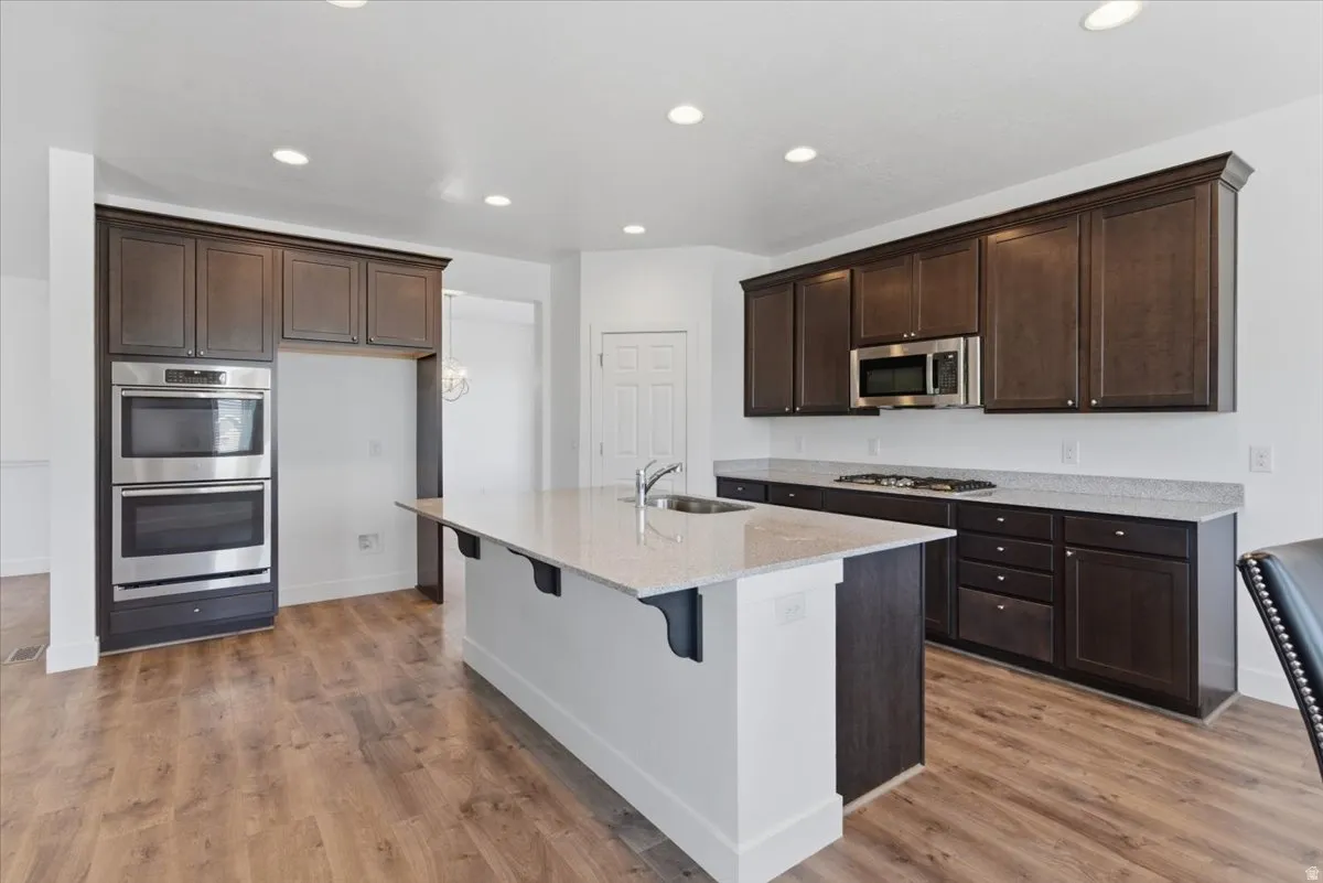 Spacious kitchen featuring an expansive center island with an undermount sink, dark wood-finish cabinetry, stainless steel double wall ovens, a built-in microwave, and wood-finish flooring