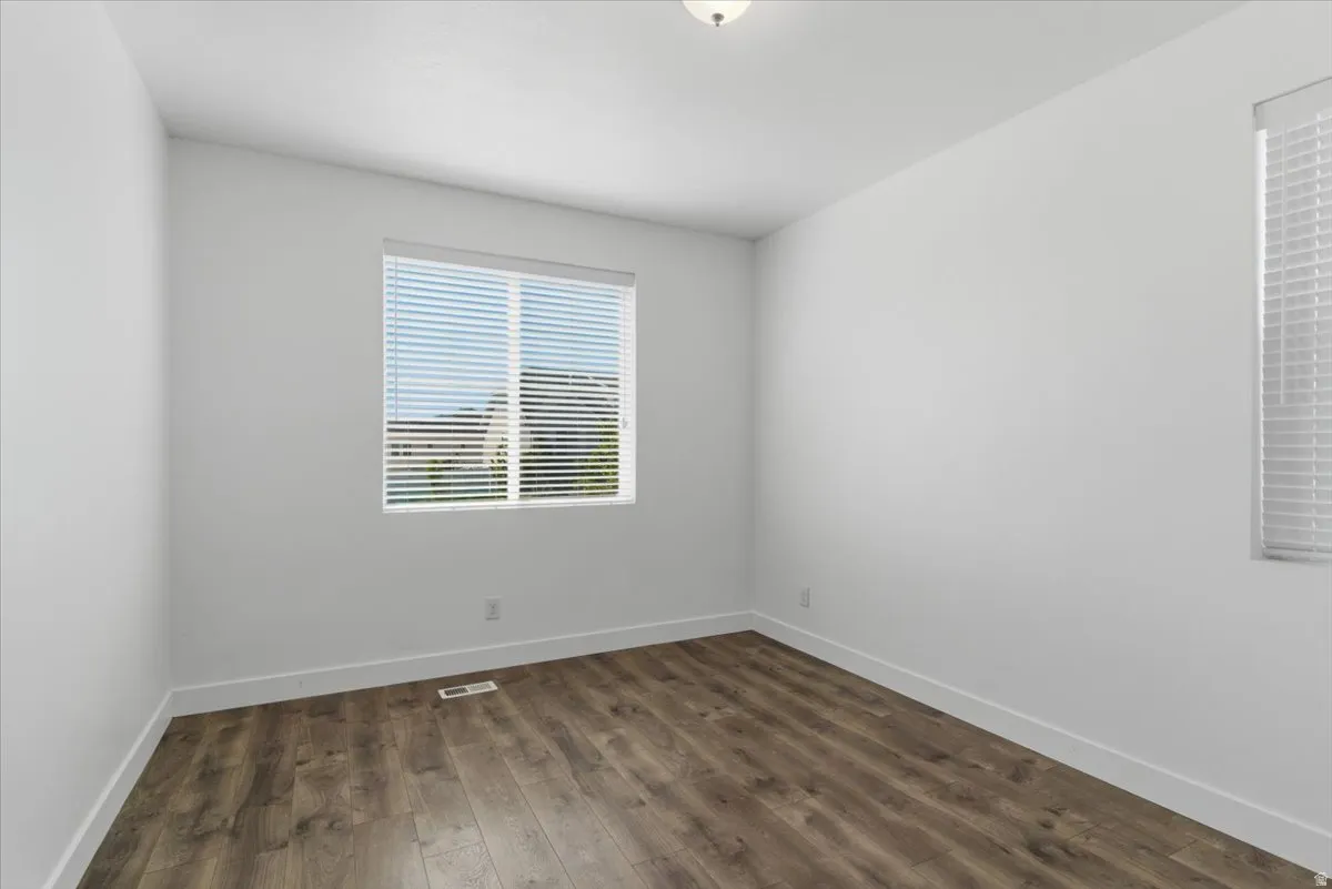 Room with wood-finish flooring, white walls, and a window featuring horizontal blinds
