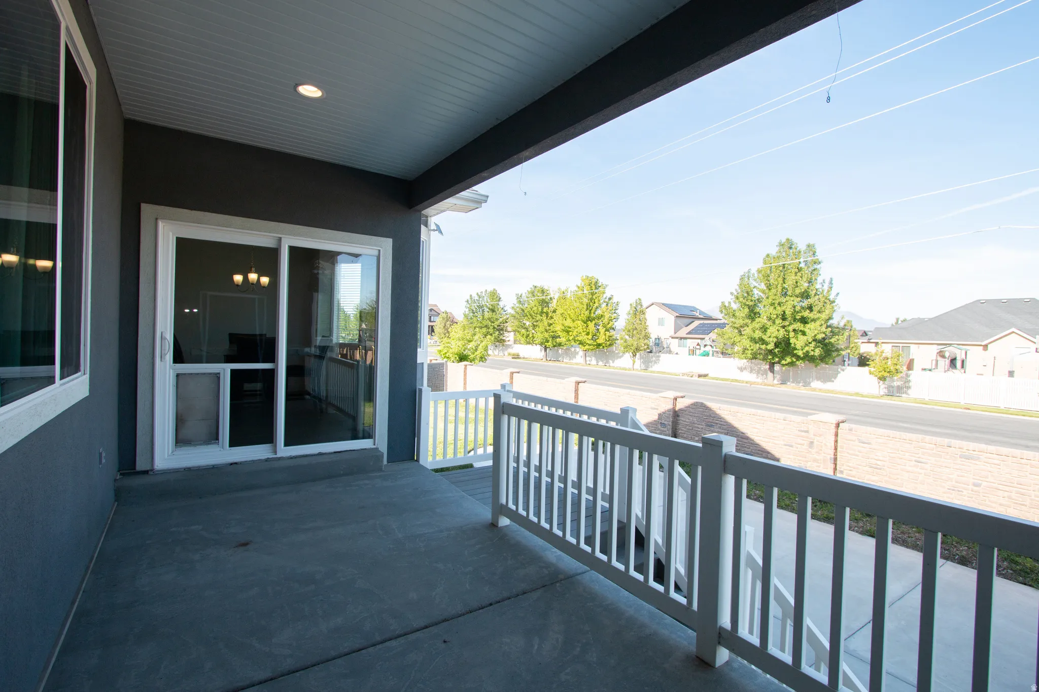 Covered patio with concrete flooring, white railing, and sliding glass door access to the interior
